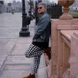 Man in denim jacket and checkered pants poses in urban Maracaibo, showcasing stylish fashion.