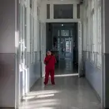 A nurse in red scrubs walks through a sunlit corridor in a hospital setting.