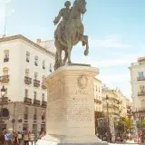 The iconic Carlos III statue in Madrid's bustling Puerta del Sol under a clear sky.