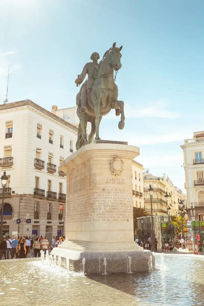 The iconic Carlos III statue in Madrid's bustling Puerta del Sol under a clear sky.