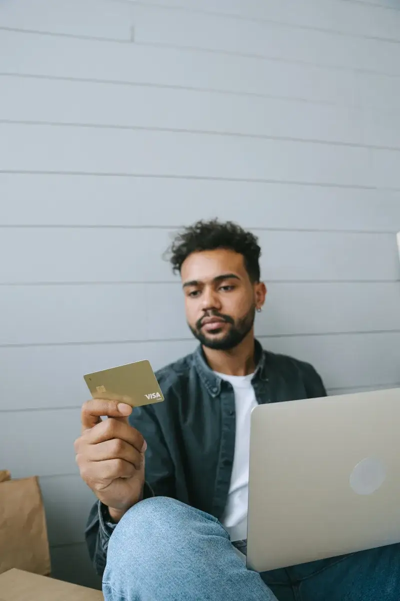 Man using Visa card for online shopping with laptop in a casual setting.