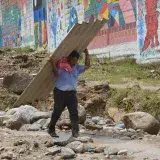 A man walks carrying a large sheet beside a colorful mural wall in Mocoa, Colombia.
