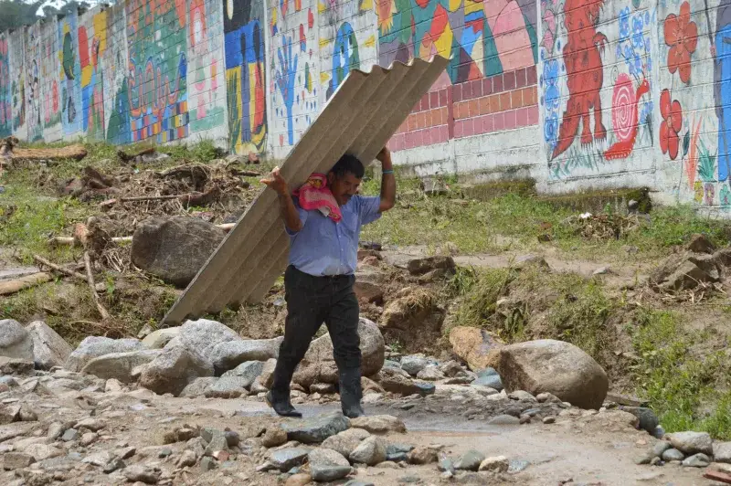 A man walks carrying a large sheet beside a colorful mural wall in Mocoa, Colombia.