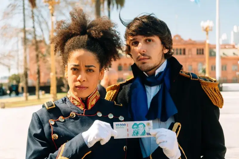 Historical reenactors in Buenos Aires costumes holding a banknote in front of Casa Rosada.