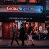 Evening view of pedestrians passing by a bustling Argentina Steakhouse in a lively urban setting.