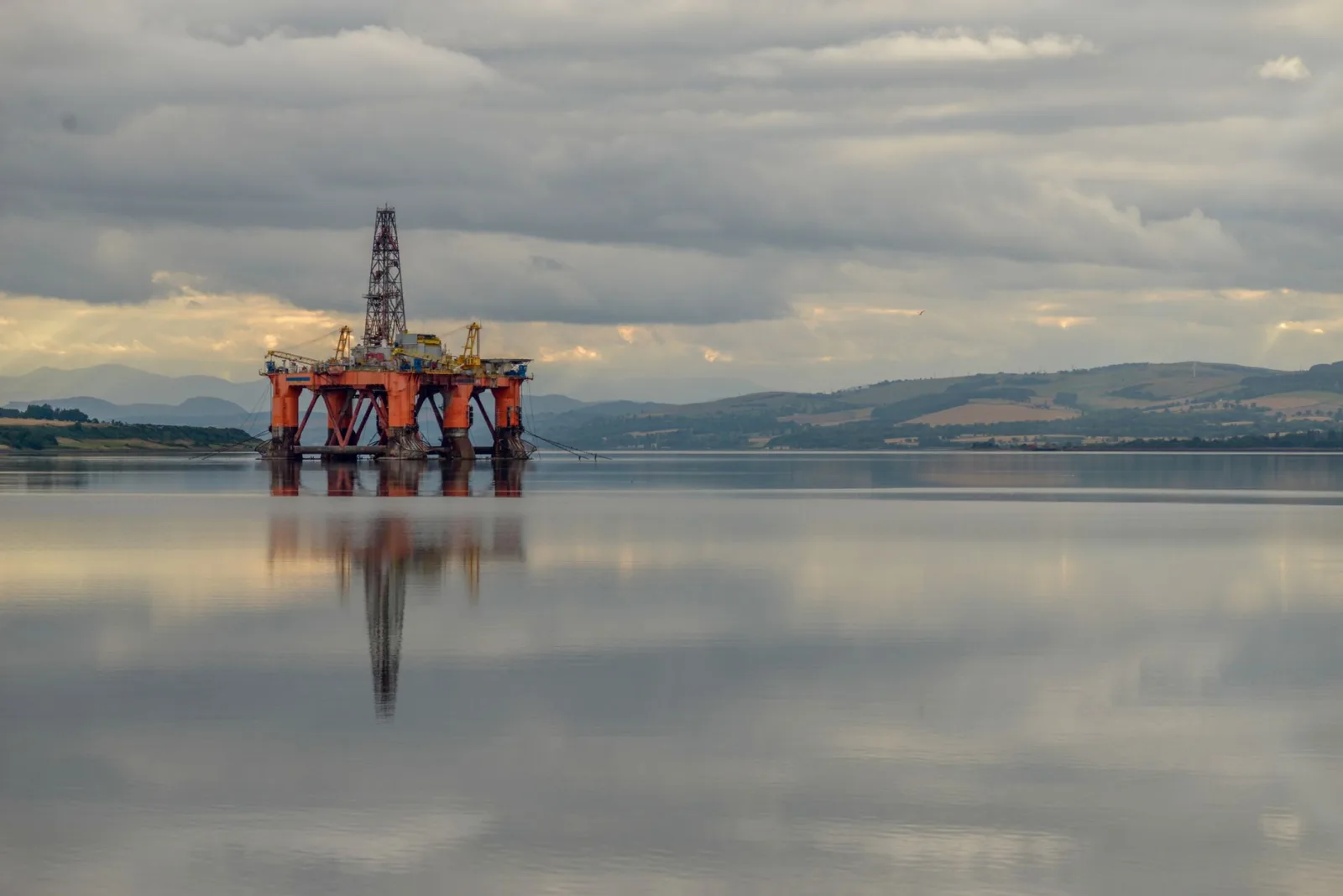 Oil drilling platform reflected on calm sea under stormy clouds in Scotland.