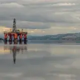 Oil drilling platform reflected on calm sea under stormy clouds in Scotland.