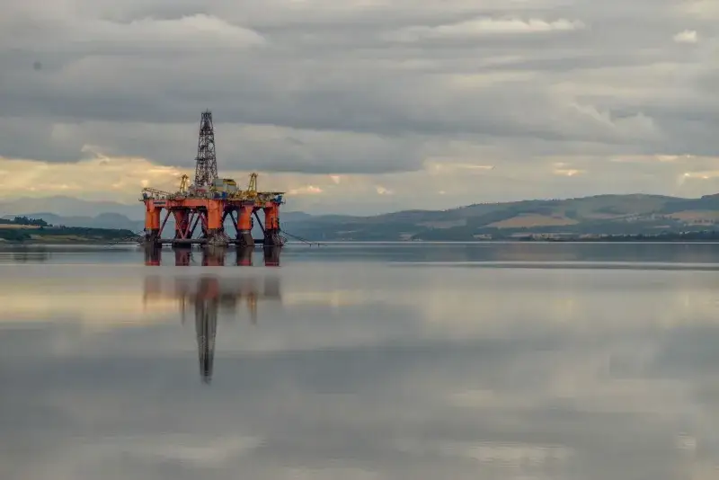 Oil drilling platform reflected on calm sea under stormy clouds in Scotland.