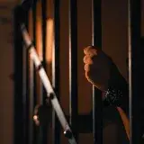 Silhouetted hand gripping jail bars, highlighting solitude and confinement.