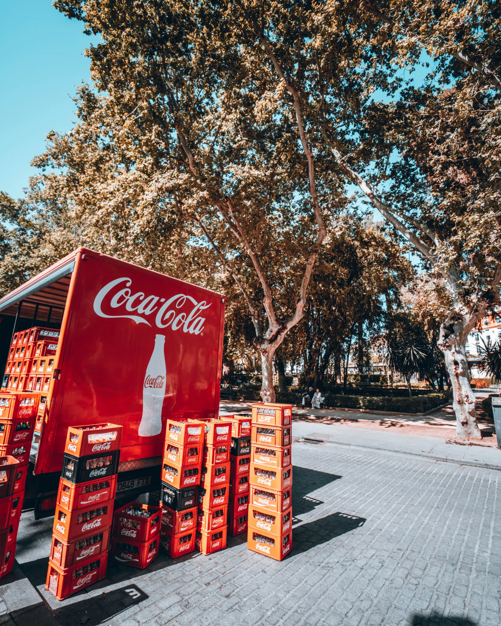 Coca-Cola truck unloading crates on a sunny street in Seville, Spain.