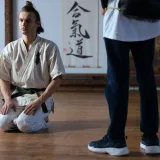Martial artist in traditional training attire kneeling in a dojo, focused and poised.