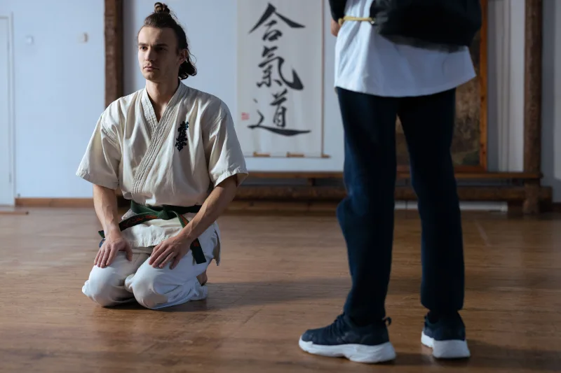 Martial artist in traditional training attire kneeling in a dojo, focused and poised.