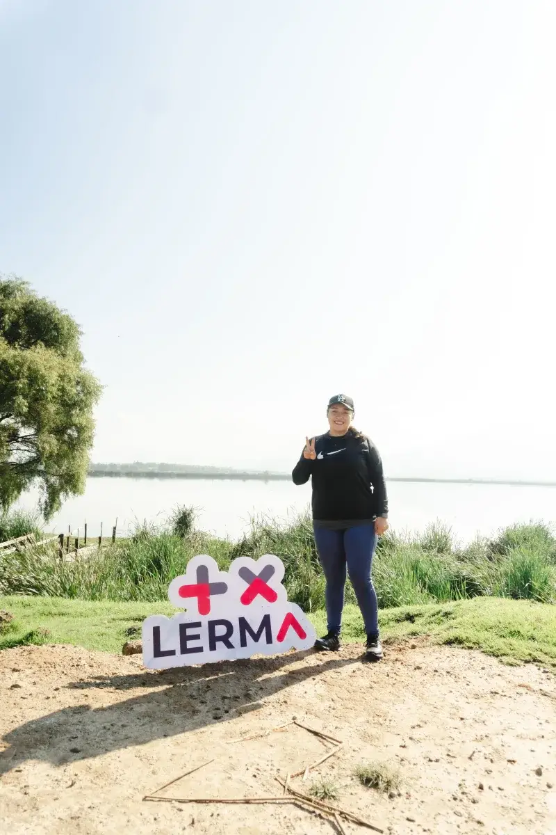 Woman smiling and posing by a sign at Lerma Lake, Santa María Atarasquillo, México.