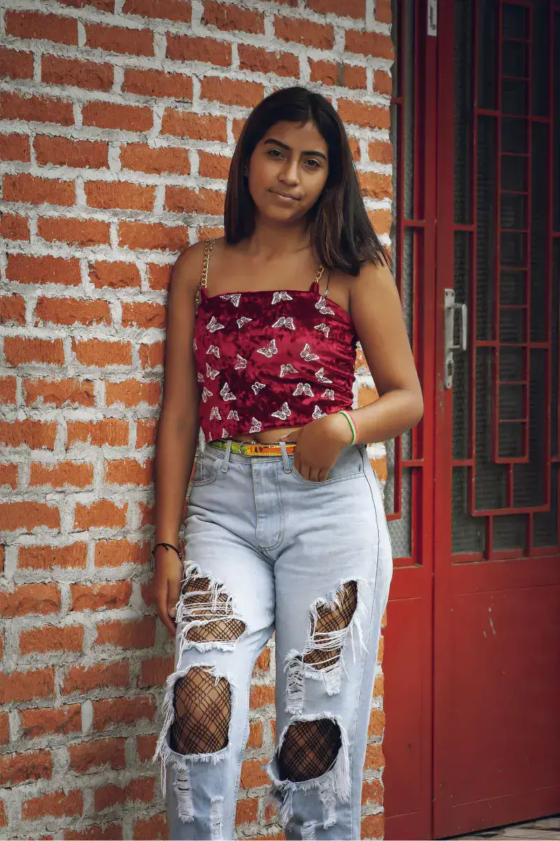 Teenage girl wearing trendy outfit in Venezuela, posing confidently by a rustic red door.