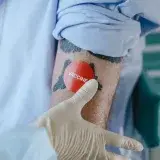 A healthcare professional applies a vaccine sticker on a tattooed arm in a medical environment.