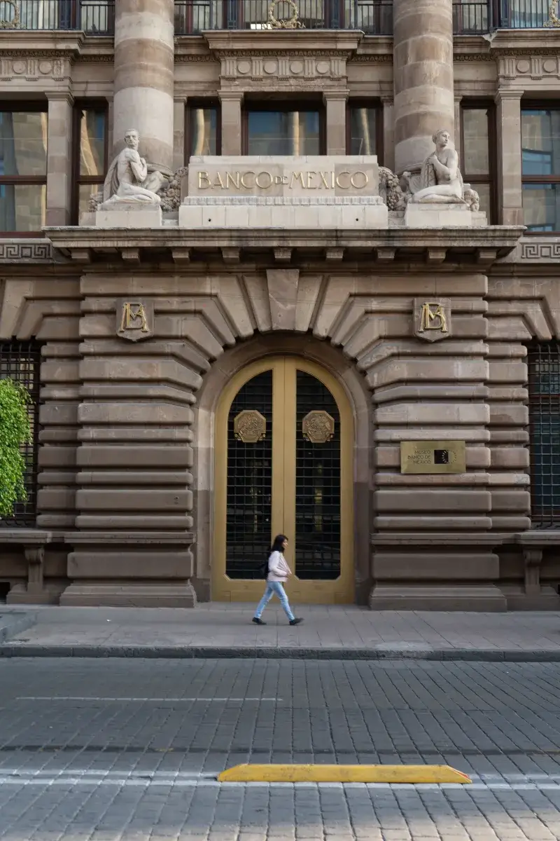 Woman walking past the Banco de México, an iconic historic facade in Mexico City.