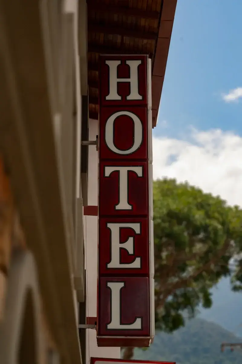 Vertical red vintage hotel sign in Mérida, Venezuela. Captured on a clear day with sky and trees in the background.