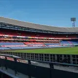Panoramic view of De Kuip stadium in Rotterdam with empty stands and a clear blue sky.