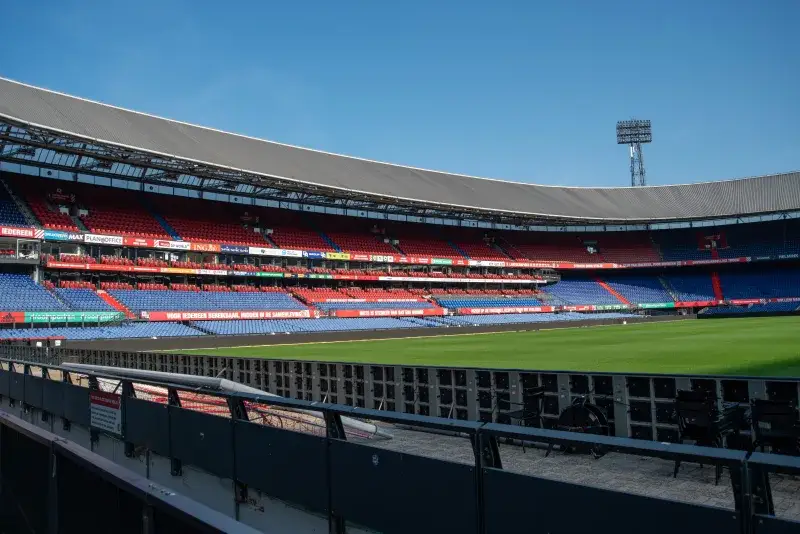 Panoramic view of De Kuip stadium in Rotterdam with empty stands and a clear blue sky.