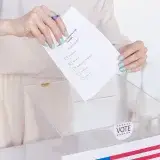 Una persona emitiendo un voto en una urna transparente durante una elección.