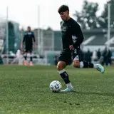 A young soccer player dribbles the ball during a daytime practice session on a grass field.