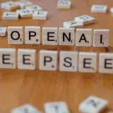 Close-up of wooden Scrabble tiles spelling OpenAI and DeepSeek on wooden table.