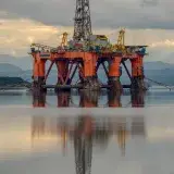 A large offshore oil rig reflects in calm waters under a cloudy sky, United Kingdom.