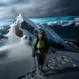 Climber on icy Andean peak near Huaraz, Peru, against dramatic sky.