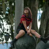 Young woman in stylish outfit sitting outdoors on a large sphere in Venezuela.
