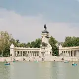 People rowing boats by the Alfonso XII monument in Buen Retiro Park, Madrid, on a sunny day.