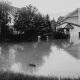 Black and white photo of suburban street flooded, houses submerged in water.