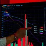 A detailed look at a male hand pointing at a graph displaying Bitcoin market trends on a digital trading screen.