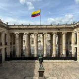 The Colombian flag waves above a historic courtyard in Bogotá, Colombia, under a clear sky.