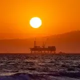 Stunning view of a silhouetted oil platform against a vibrant orange sunset over Huntington Beach, California.