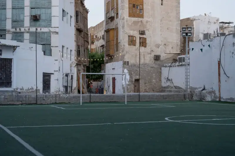 An empty soccer field in the heart of Jeddah's historic district, surrounded by traditional architecture.