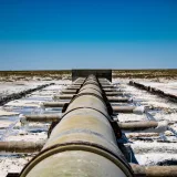 Large industrial pipeline discharging wastewater in arid, rural landscape under clear blue sky.