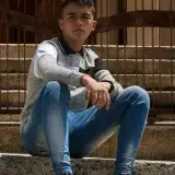 Casual portrait of a young man sitting on outdoor steps in Venezuela. His serious expression and modern clothing add depth to the shot.