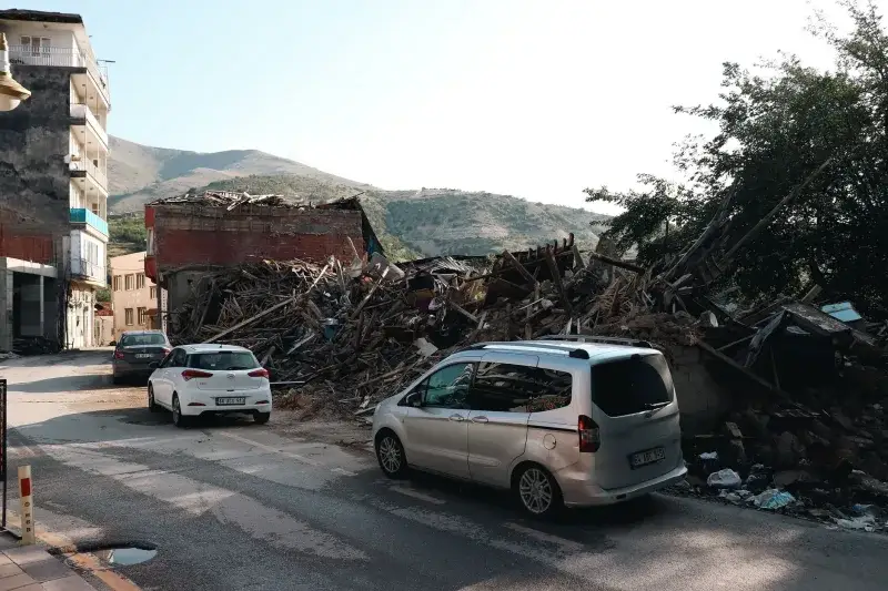 A city street with cars passing by buildings destroyed by an earthquake.