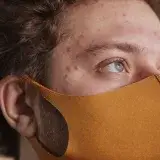 Detailed close-up of a man wearing a face mask, highlighting his acne and blue eyes.