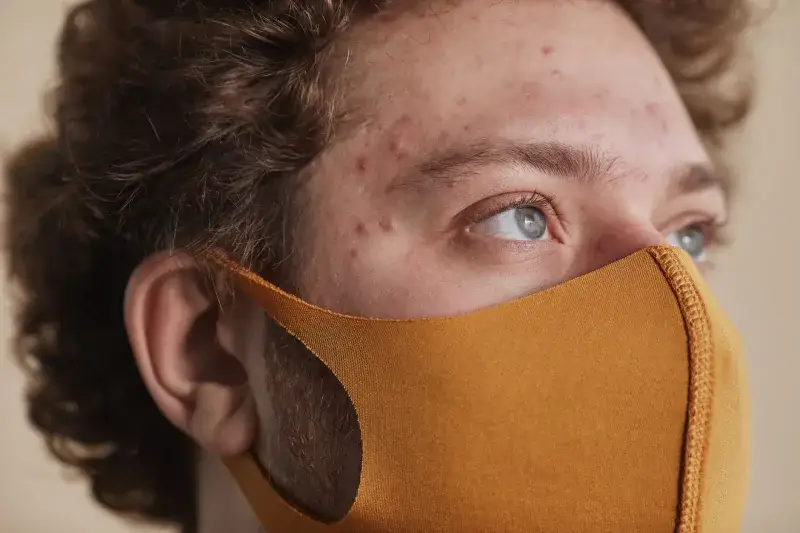 Detailed close-up of a man wearing a face mask, highlighting his acne and blue eyes.