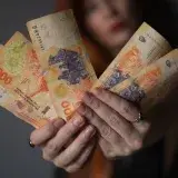Primer plano de una persona sosteniendo billetes de peso argentino, mostrando los detalles de la moneda.