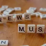 Primer plano de fichas de letras de madera sobre una mesa que forman la palabra “News Musk”, concepto de cobertura mediática.