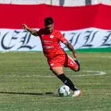 Action-packed moment of a soccer player in red during a competitive match on a green field.