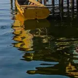 A rustic boat floats beside a wooden pier at sunset in Maracaibo, Venezuela, creating serene reflections.
