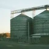 Large metal silos in a rural industrial area at sunset.
