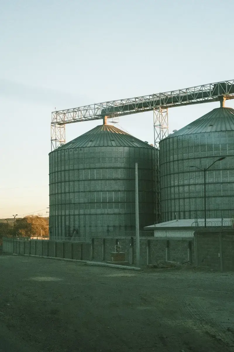 Large metal silos in a rural industrial area at sunset.