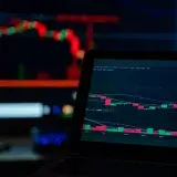 A dimly lit desk setup displaying cryptocurrency trading charts on multiple screens.