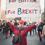 Woman in red jacket holding a 'For Britain For Brexit' sign during a protest in London.