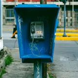 Vandalized blue payphone in Venezuela, surrounded by urban street scenery.