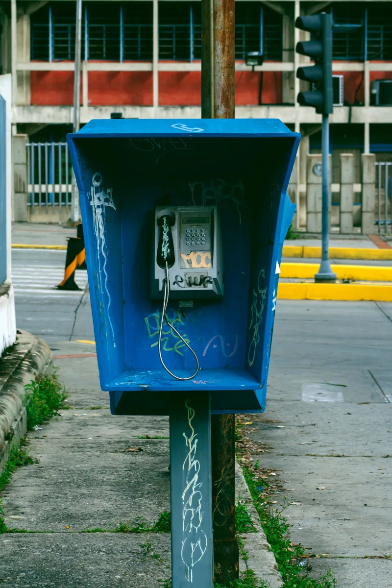 Vandalized blue payphone in Venezuela, surrounded by urban street scenery.